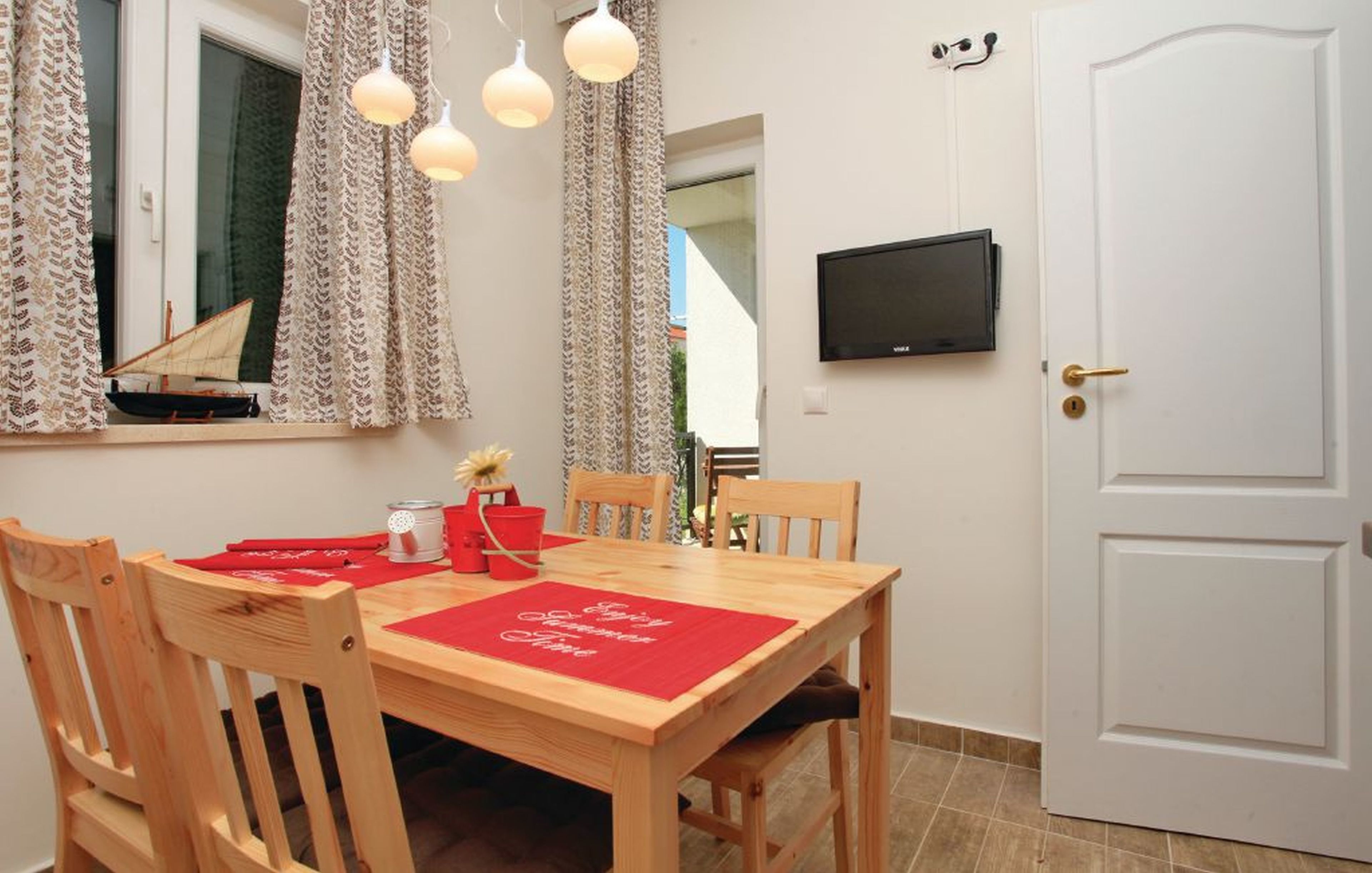 A dining area with a wooden table, red placemats, and a television mounted on the wall.