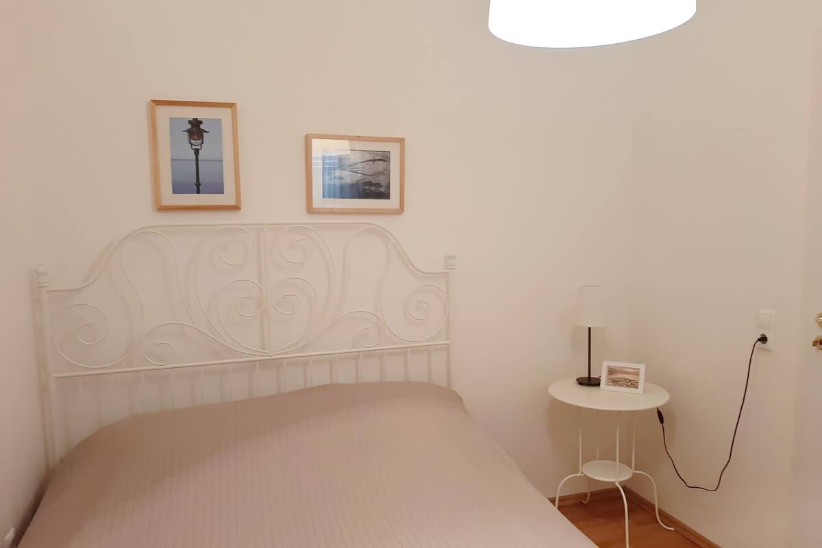 A bedroom with a bed, a bedside table with a lamp, and two framed pictures on the wall.