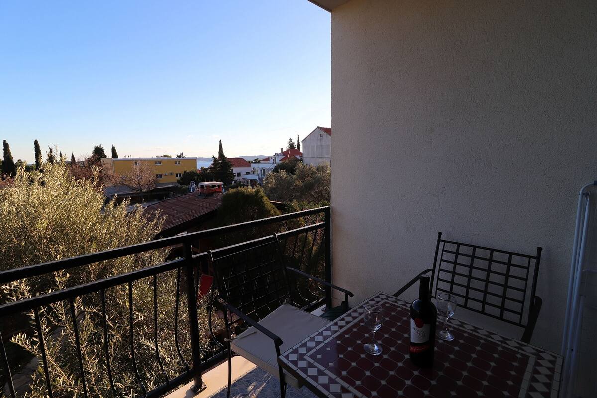 A balcony with a table and chairs, overlooking a residential area with houses and trees.