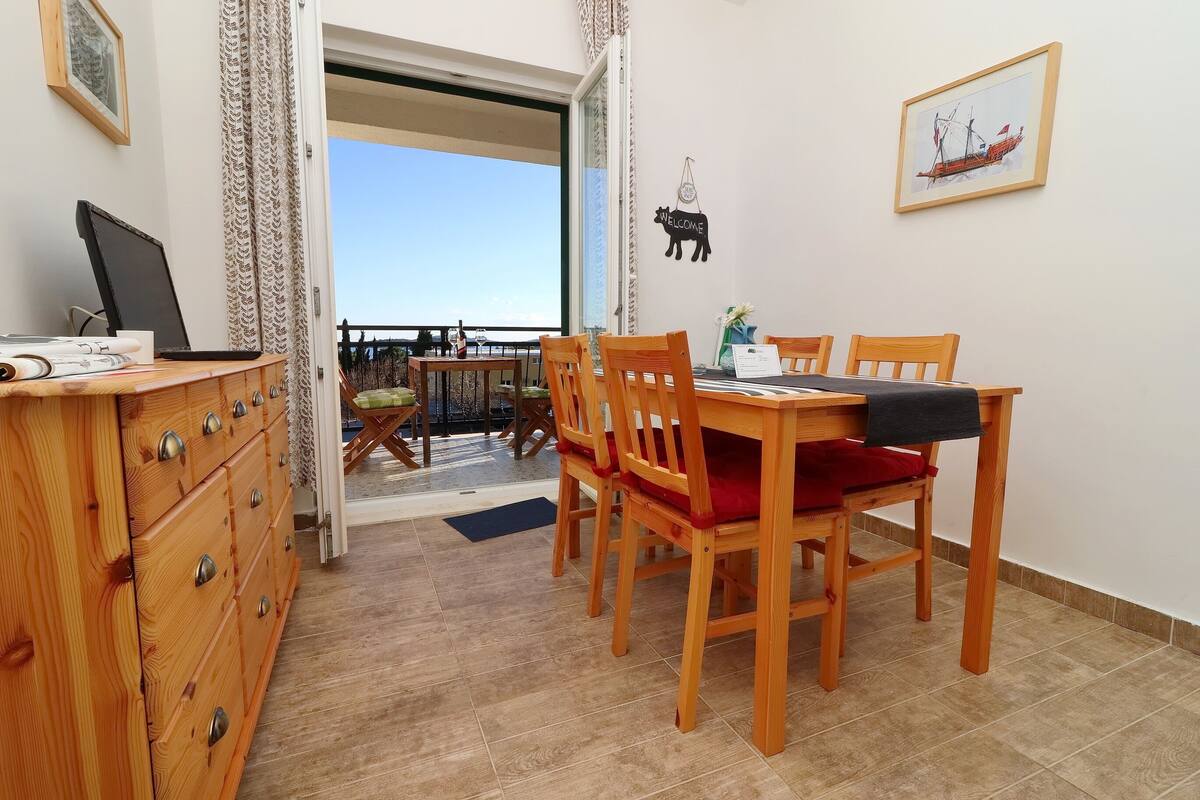 A room with a wooden dining table and chairs, a wooden dresser, a computer, and a view of the outdoors.