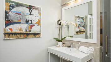 A modern bathroom with a white sink, a large mirror, and a colorful abstract painting on the wall.