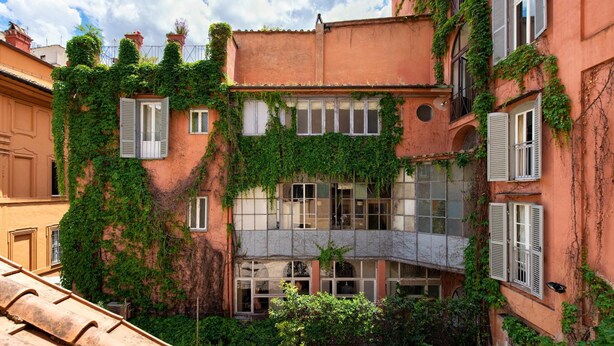 Une cour intérieure avec un bâtiment recouvert de lierre, doté de nombreuses fenêtres et d’un petit pont.