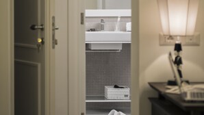 Un couloir menant à une salle de bain équipée d’un lavabo, d’un miroir et d’une serviette posée sur le sol.