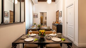 Un coin repas avec une longue table dressée pour le repas, un miroir sur la gauche et une porte portant le numéro « 5 » sur la droite.