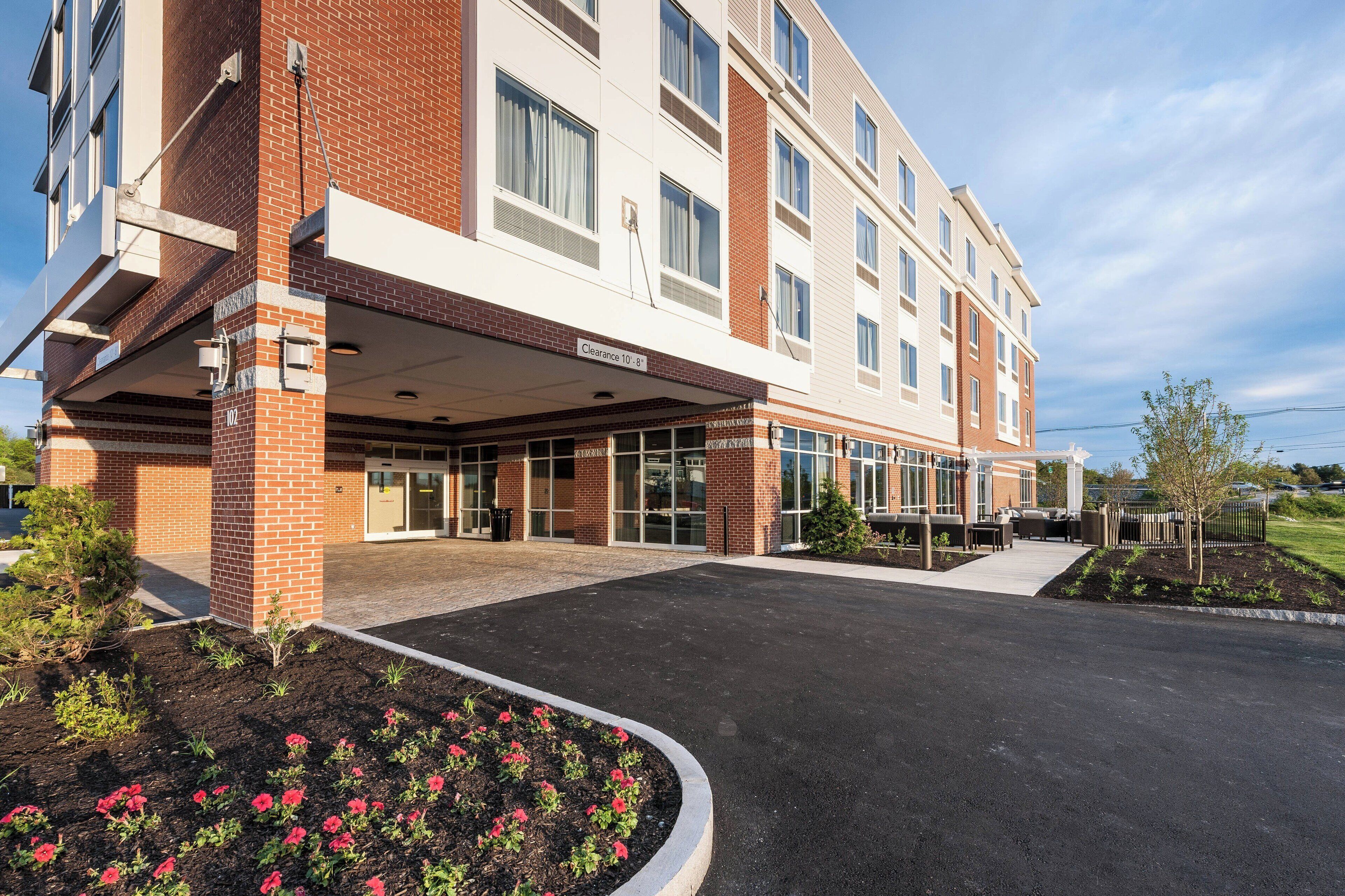 A multi-story hotel with a brick facade, a covered entrance, and a landscaped area with flowers.