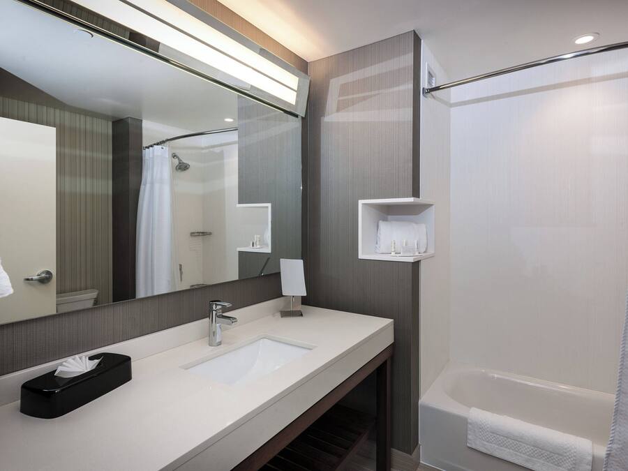 A modern bathroom with a large mirror, a sink, a shower, and a towel rack.