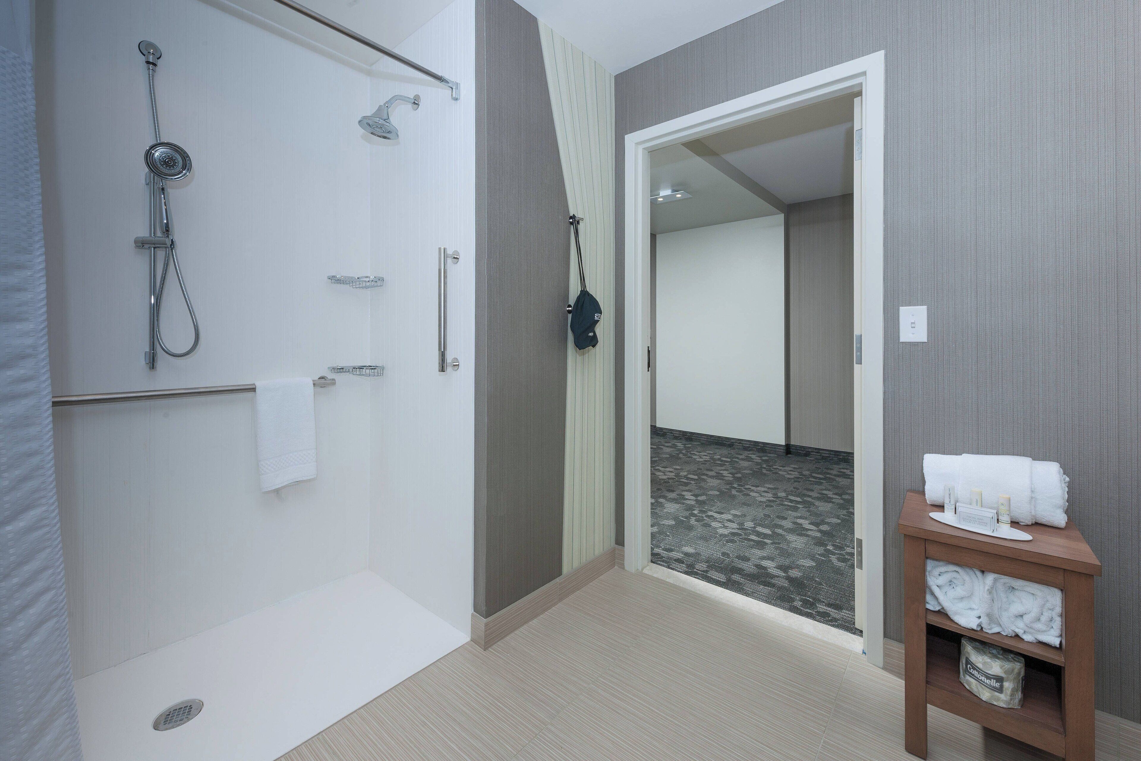 A modern bathroom with a shower, a towel rack, and a small shelf with towels.