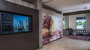 Un hall d’hôtel moderne doté d’un écran numérique affichant l’indice composite de la Bourse de New York, d’un grand tableau abstrait au mur et d’un espace détente avec des canapés et une table basse.