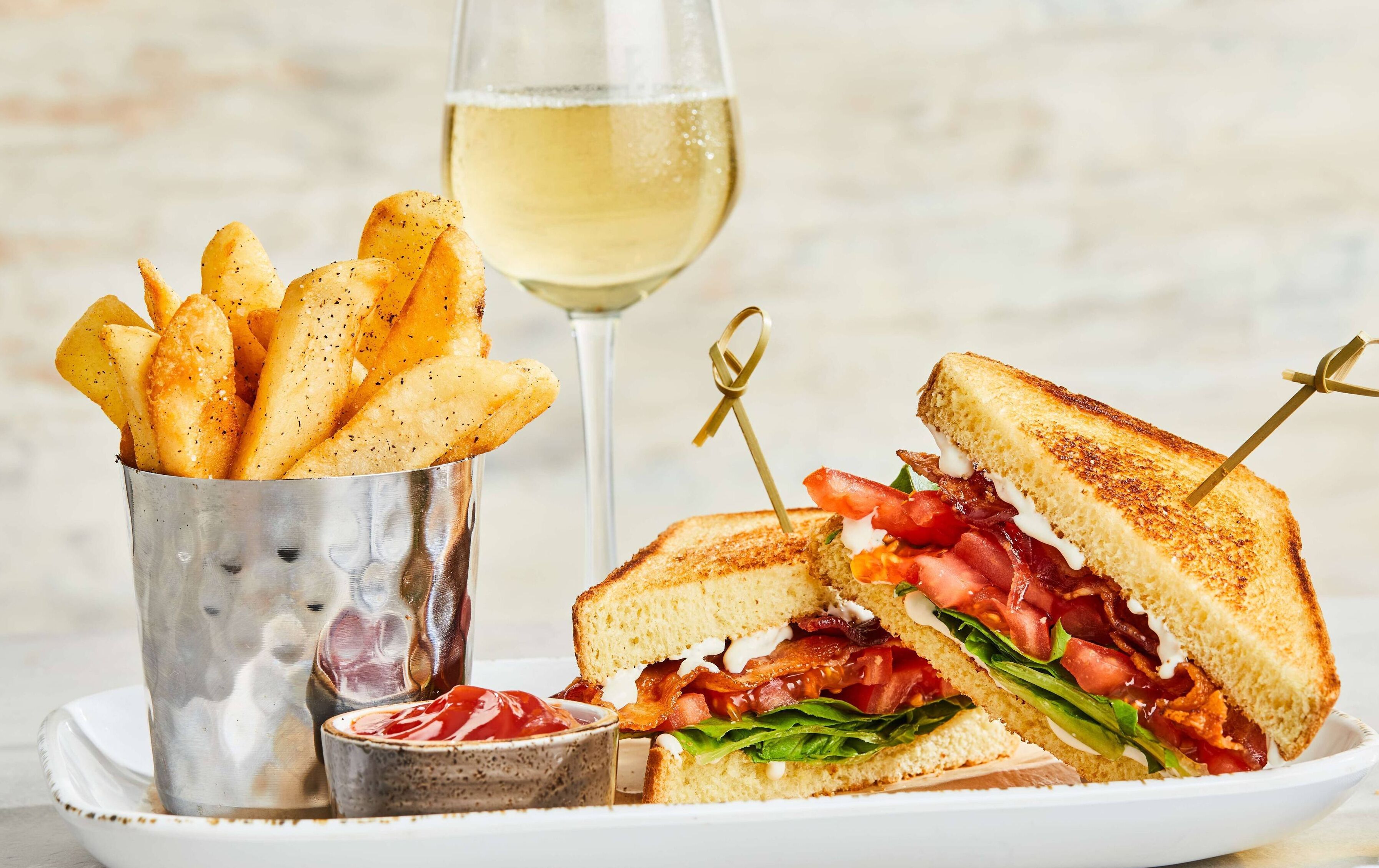 Un sandwich accompagné d’une portion de frites et d’un verre de vin blanc.