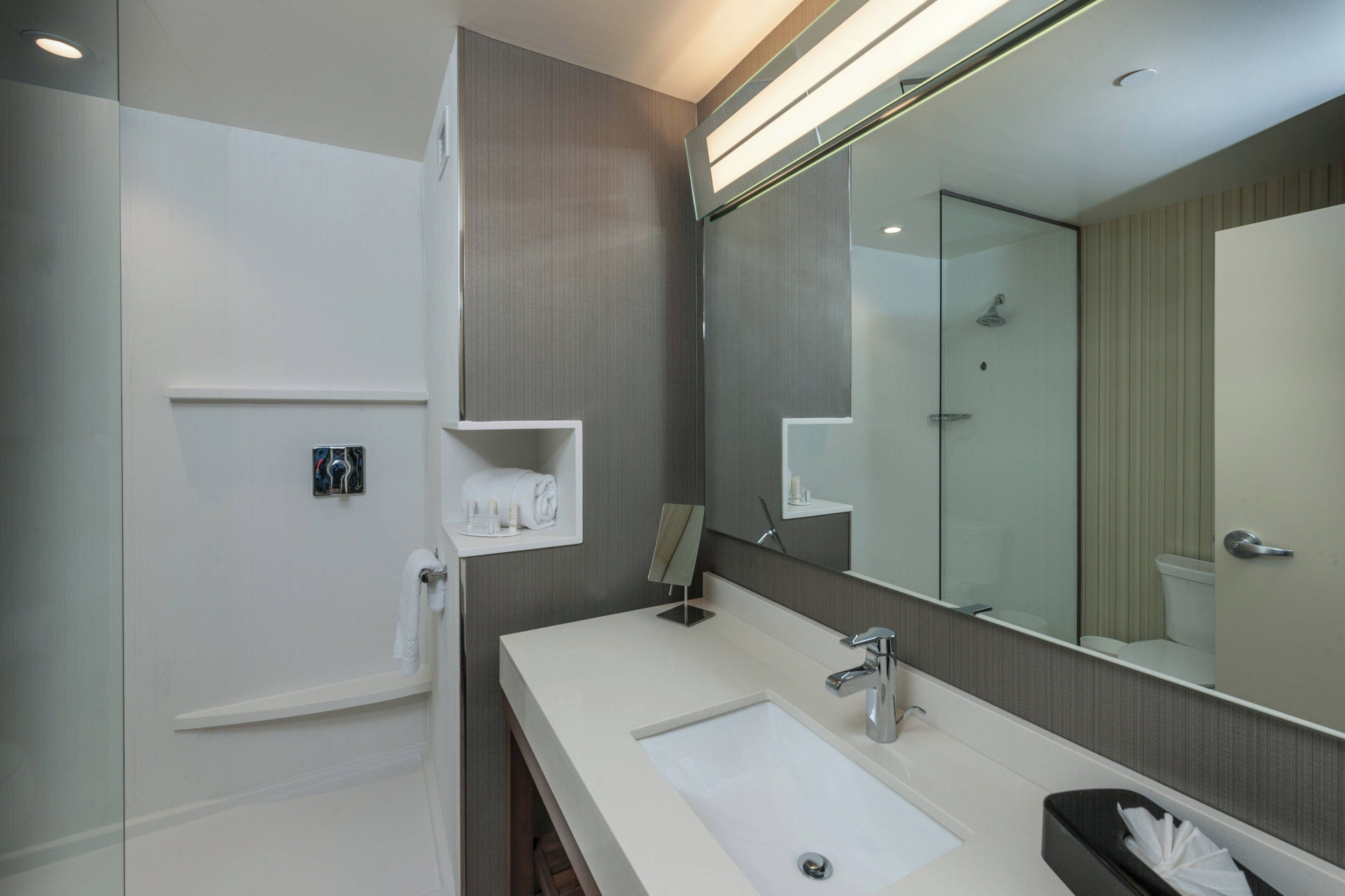 A modern bathroom with a large mirror, a sink, and a shower.
