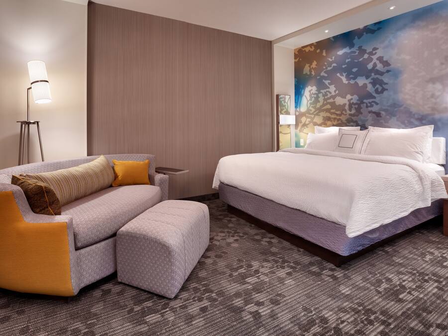A hotel room with a bed, a sofa, a small table, and a lamp.