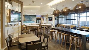 Um restaurante moderno com mesas altas, banquetas e iluminação pendente.