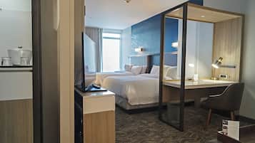 A hotel room with a bed, a desk, a chair, a mirror, and a small table with a sign.
