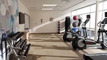 A gym with exercise equipment, a wall-mounted TV, and large windows.