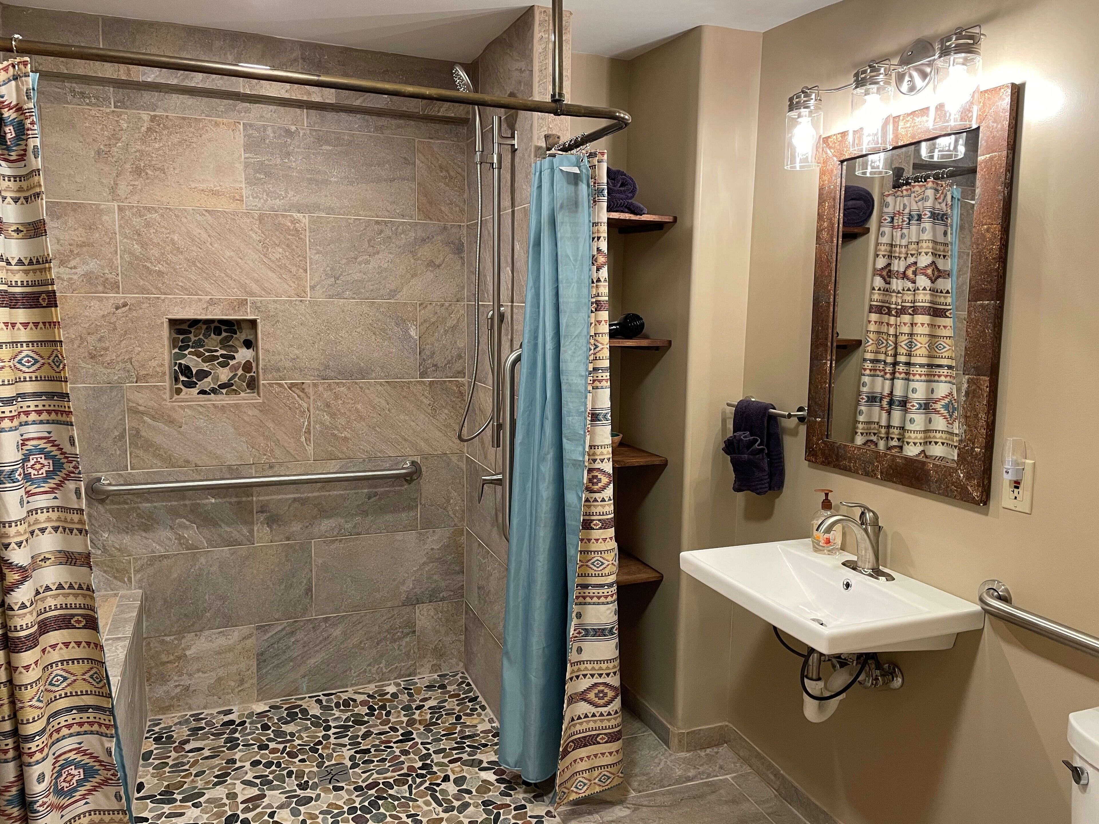 A bathroom with a walk-in shower, a sink, a mirror, and a towel rack.