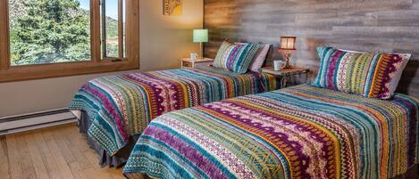 A room with two beds, a large window, a wooden headboard, and a wall-mounted lamp.