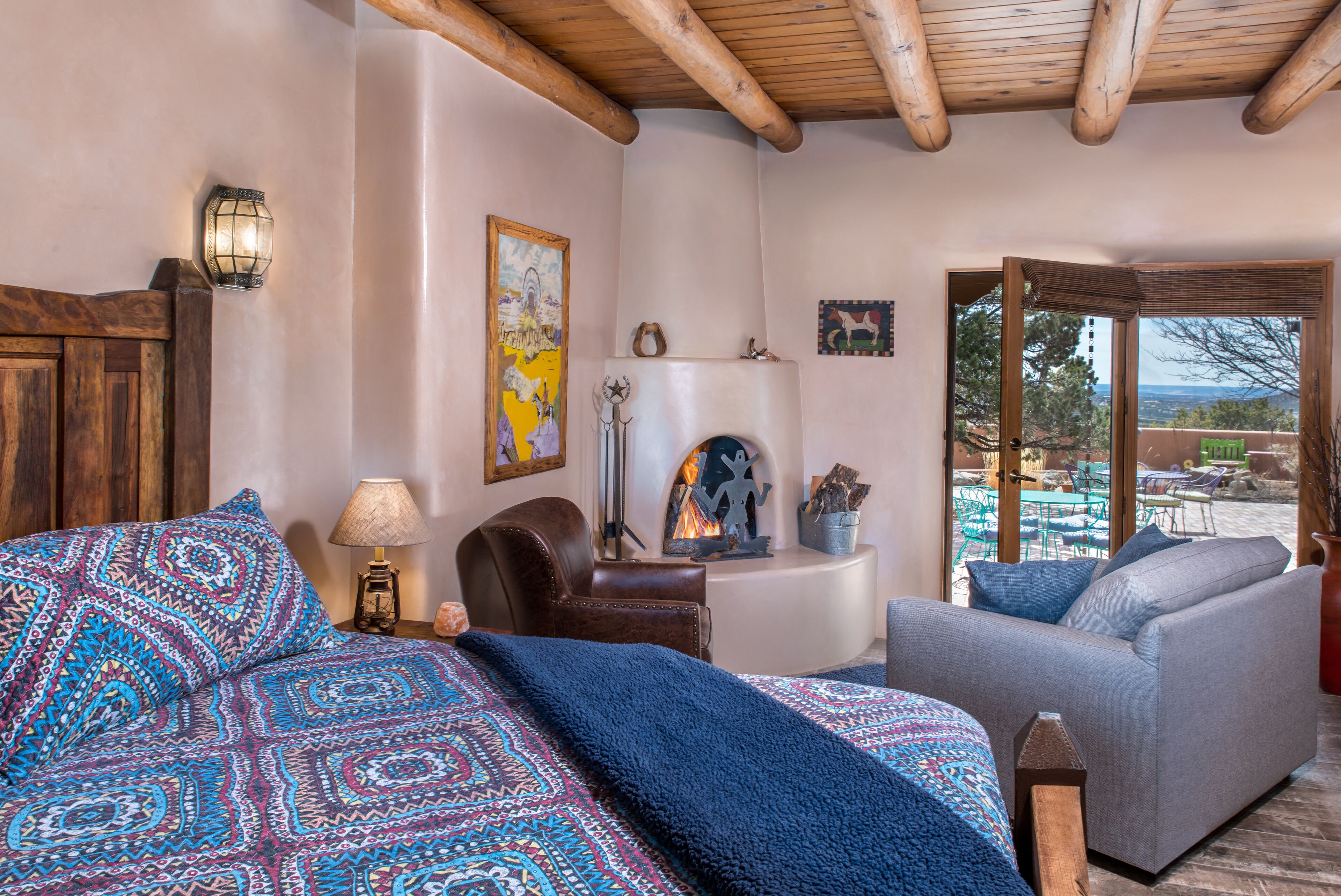 Ein Schlafzimmer mit Bett, Sessel, Sofa, Kamin und Blick ins Freie.
