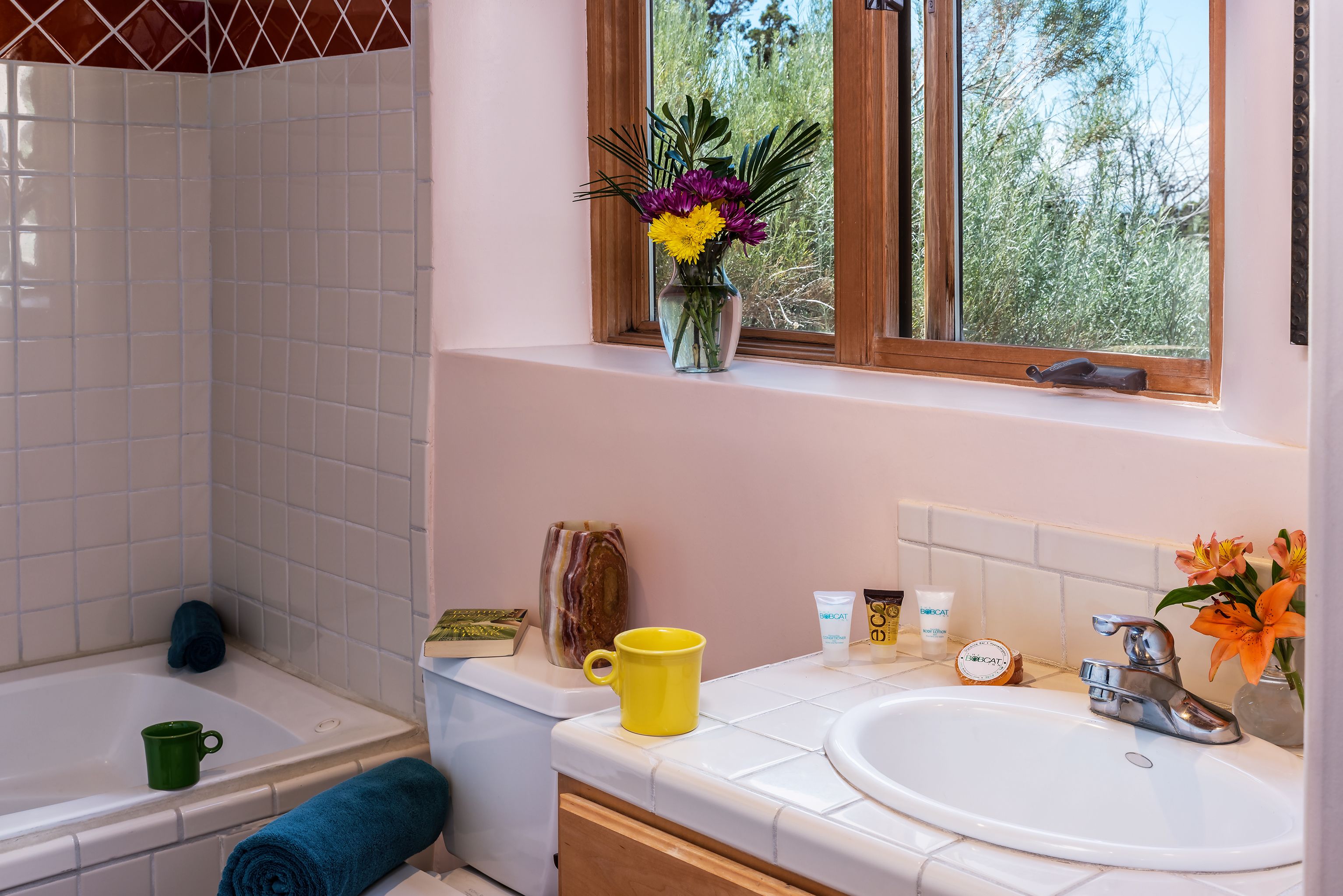 A bathroom with a bathtub, a sink, and a window with a view of trees.