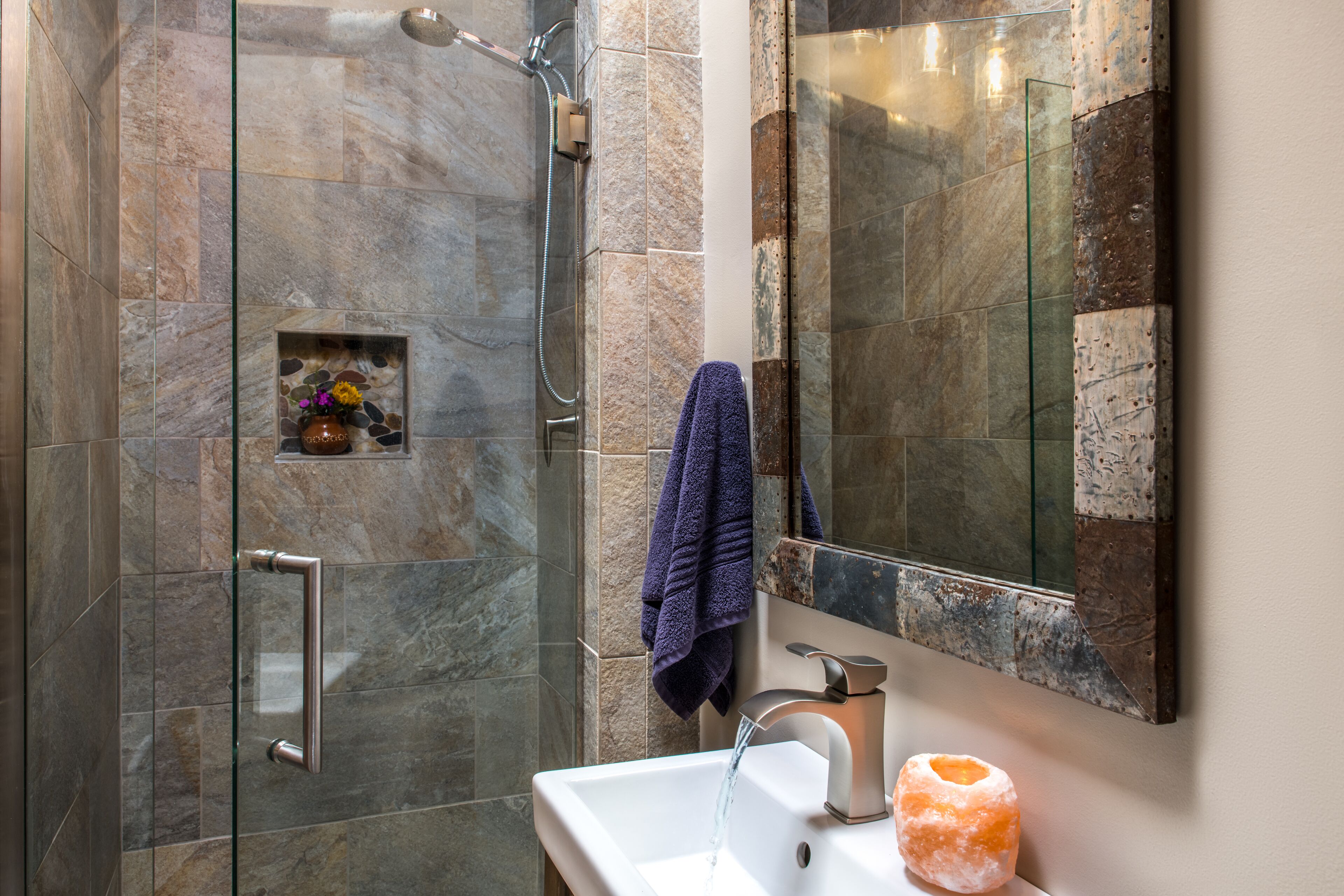 A modern bathroom with a glass shower enclosure, a white sink, and a decorative stone shelf.