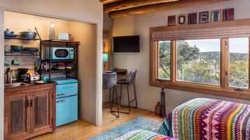 Una cocina compacta con un electrodoméstico azul, un taburete de bar y un televisor en la pared.