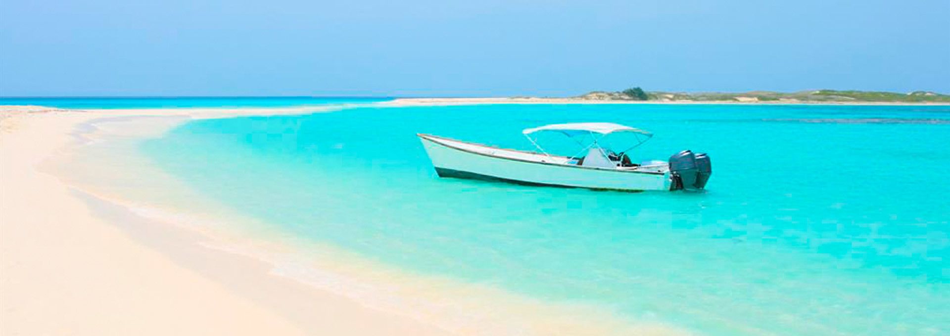 A boat on a clear turquoise sea with a sandy beach in the background.
