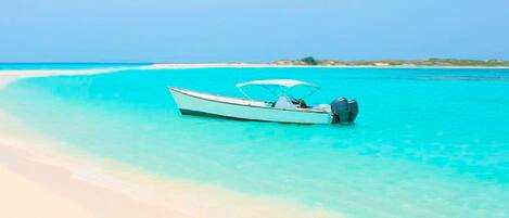 A boat on a clear turquoise sea with a sandy beach in the background.