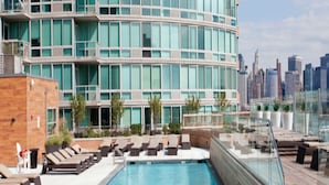 A rooftop pool with lounge chairs and a city skyline in the background.