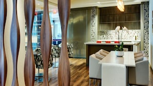 A modern dining area with a wooden floor, a central table with chairs, and a kitchen in the background.