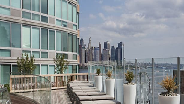 A rooftop terrace with a wooden deck, seating areas, potted plants, and a city skyline view.