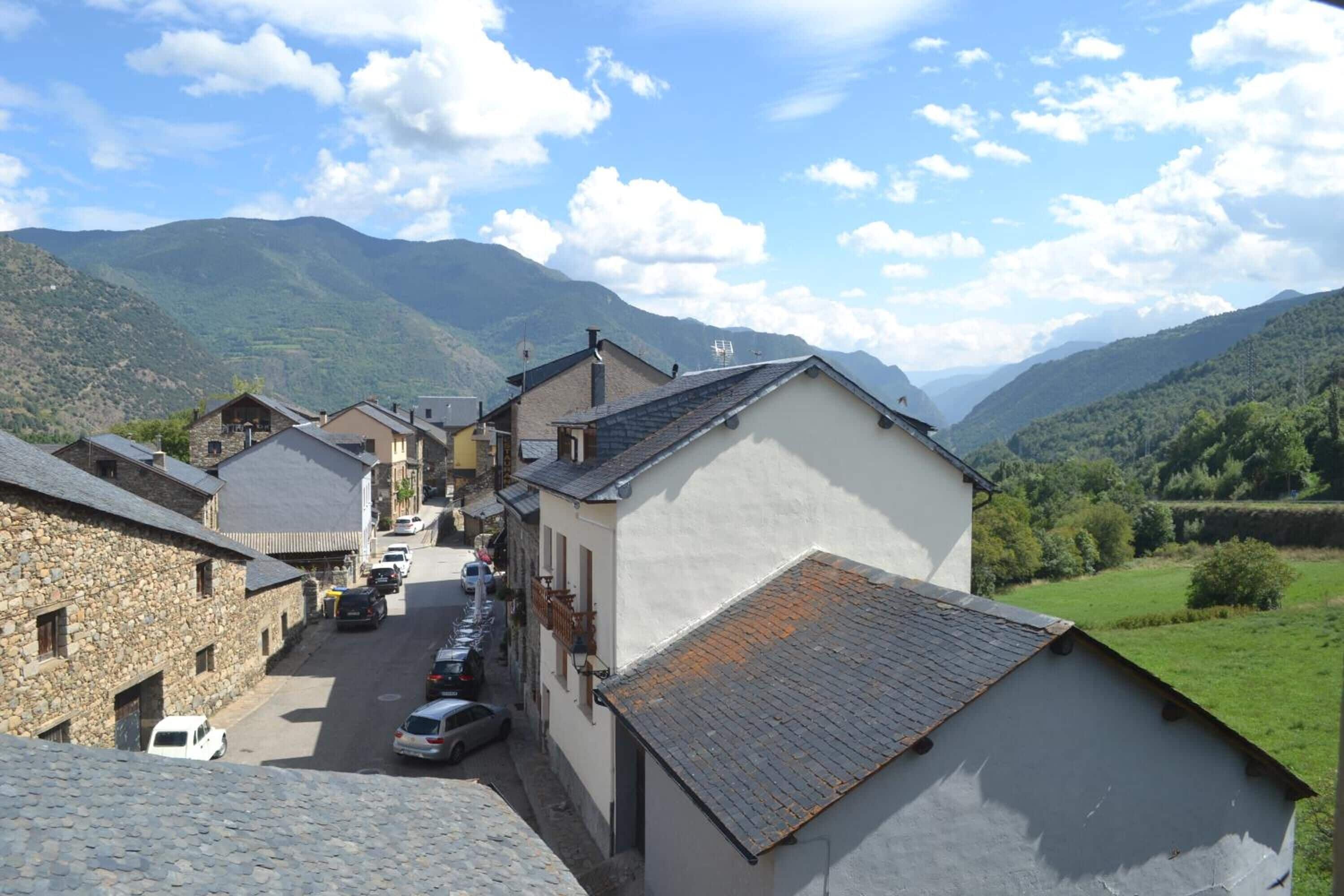 Una calle estrecha en un pueblo montañoso con edificios de piedra y coches aparcados.