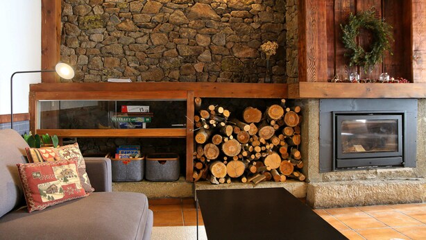 Una sala de estar acogedora con pared de piedra, chimenea y leñera.