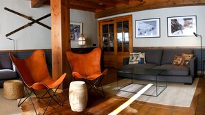 Una sala de estar acogedora con techo de madera, un sofá gris, dos sillones de cuero naranja, una pequeña mesa de madera y una cesta tejida.
