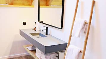 Ein modernes Badezimmer mit Dachfenster, einer Holzleiter zum Abtrocknen der Handtücher, einer weißen Toilette und einem fest installierten Waschbecken mit Spiegel darüber.