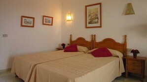 Una cama doble con cabecera de madera, dos mesitas de noche y tres cuadros enmarcados en la pared.