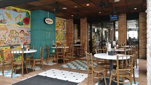 Un café al aire libre con mesas y sillas de madera, un mural colorido en la pared, y un letrero que dice "Myloft".