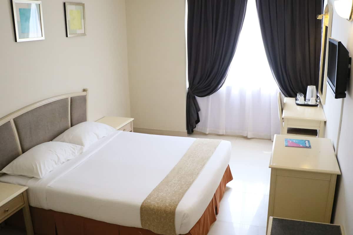 A hotel room with a bed, bedside table, and a small desk with a chair.