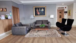 Un vestíbulo moderno con mostrador de recepción, sofás grises, una silla negra, una mesa de centro y un cuadro en la pared.