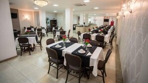 A dining area with tables set for service, a kitchen in the background, and a chandelier. - Francisco Beltrao Palace (Francisco Beltrao)