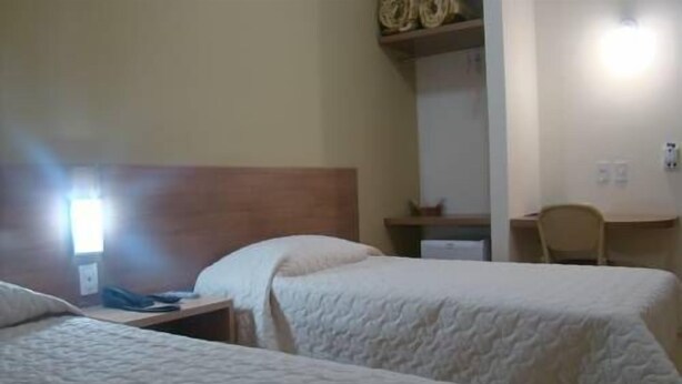 A hotel room with two beds, a desk, a chair, and a shelf with decorative items. - Francisco Beltrao Palace (Francisco Beltrao)