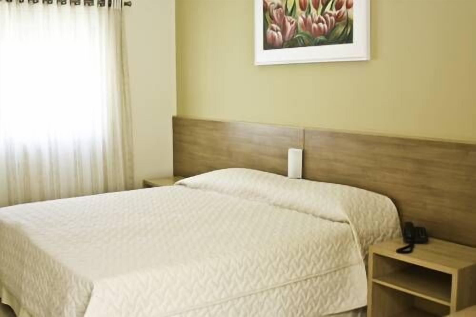 A hotel room with a bed, a nightstand, a telephone, and a painting on the wall.