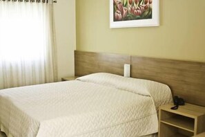 Una habitación de hotel con cama, mesita de noche, teléfono y un cuadro en la pared.