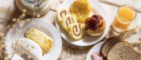 Een ontbijttafel met brood, gebak, ham en een kop koffie.