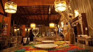A restaurant interior with wooden tables, hanging wicker chandeliers, and a colorful tablecloth. - Vivá Barra Hotel Pousada (Barra de São Miguel)