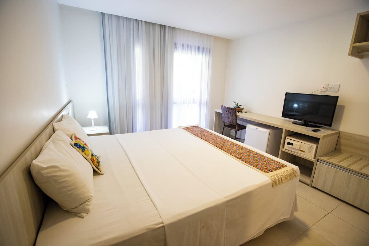 Une chambre d’hôtel avec un lit, un bureau avec une télévision, une chaise et une petite table.