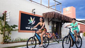 Two people on bicycles in front of a building with a sign for 'Hotel Pousada Viva Barra'.