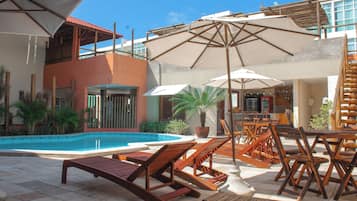 Relax by the pool surrounded by lounge chairs and umbrellas, with a balcony offering a view of the clear blue waters.