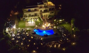 A large outdoor swimming pool surrounded by a crowd of people, with a building in the background. - Villa Artemis (Rhodes)