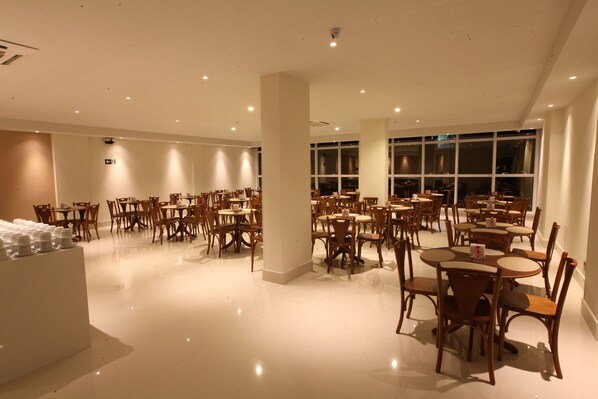 A spacious restaurant with multiple dining tables and chairs, a clean floor, and large windows.