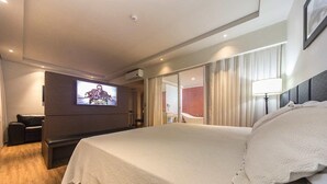 Une chambre d’hôtel moderne dotée d’un grand lit, d’un téléviseur à écran plat fixé au mur, d’un coin salon avec un canapé et d’une grande fenêtre avec des rideaux.