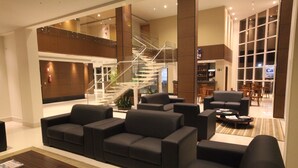 Un hall d’entrée moderne avec un escalier, des canapés noirs, une table basse et un espace d’accueil.